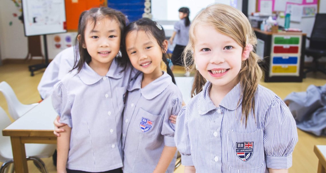 Three young female students from our Spotlight School are smiling at the camera in a classroom in Thailand