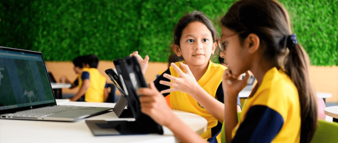 Two female students sit at a desk with technology