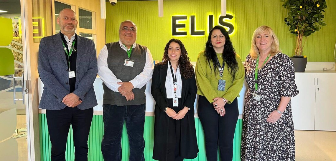 Five educators stand in a school foyer, smiling at camera